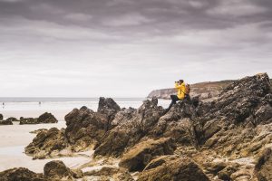 Young woman wearing yellow rain jacket at the beach, looking through binoculars, Bretagne, France